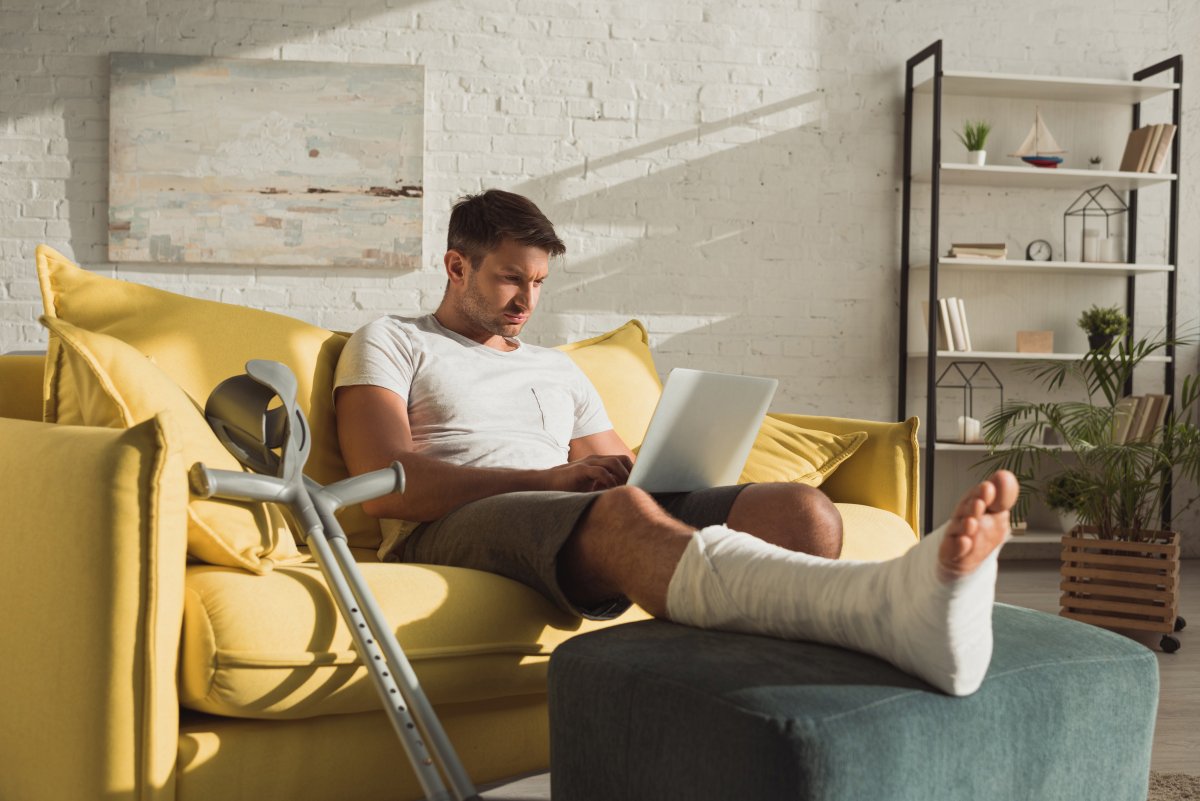 Een man heeft zijn been gebroken, rust uit in de zetel terwijl hij op de computer bezig is.