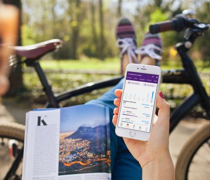 Fille reposant ses pieds sur un vélo, tenant un magazine et faisant défiler une application mobile. 